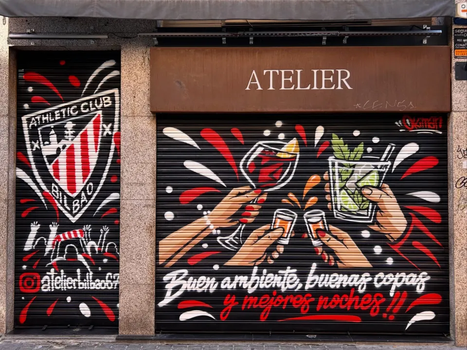 Dos persianas de un bar: el escudo del Athletic y unas manos brindando con copas y cócteles