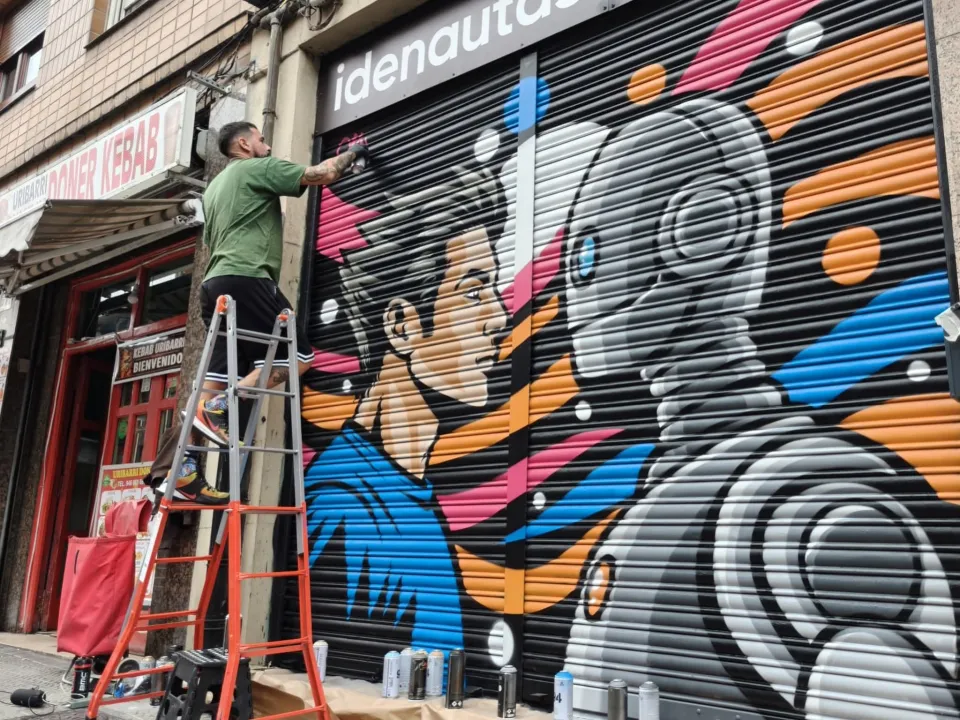 Okiman subido a una escalera, pintando con spray una persiana