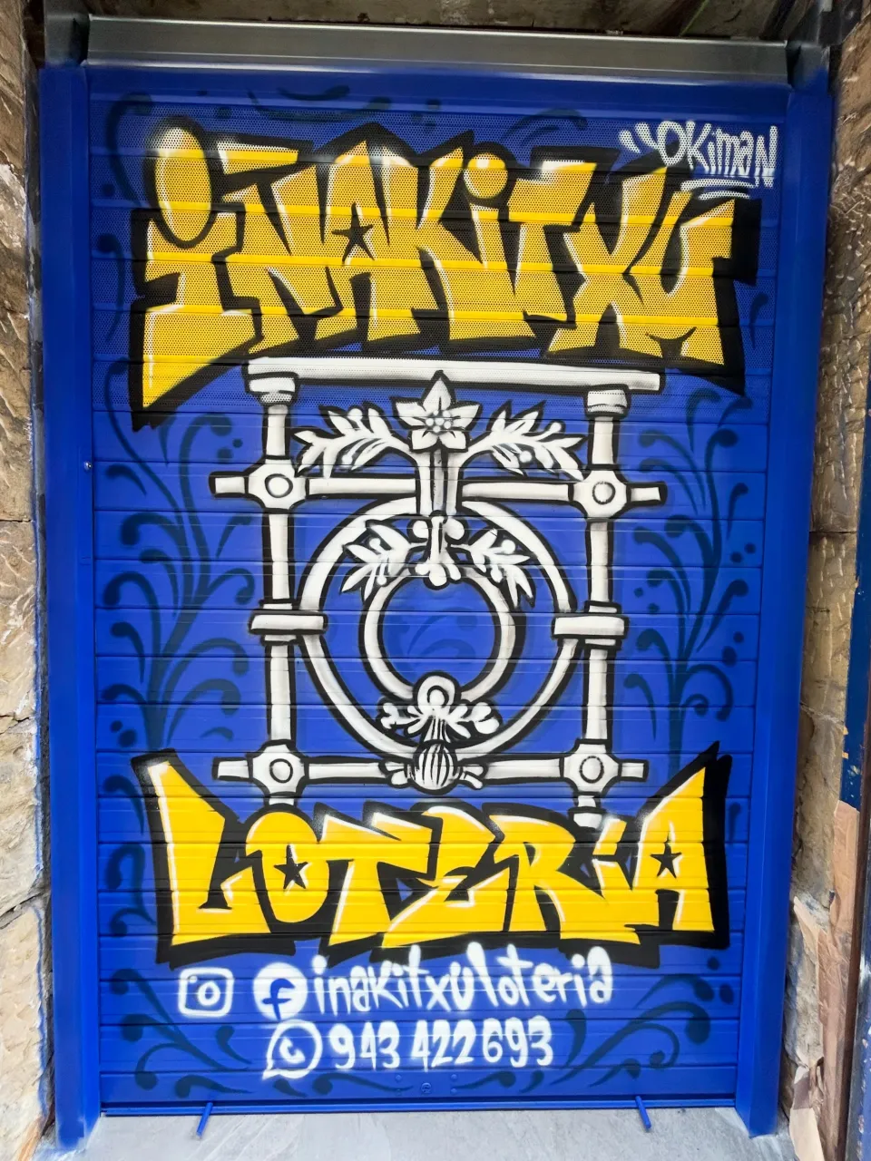 Persiana azul de una administración de lotería con un rótulo amarillo y un motivo de forja