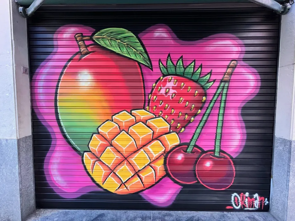 Persiana negra pintada con un mango, fresas y cerezas sobre fondo rosa