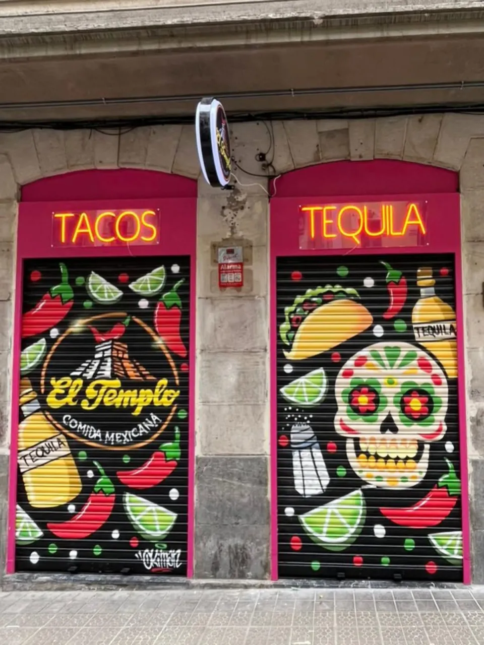 Dos persianas rosas de un restaurante mexicano, con tacos, chiles, limas y una calavera