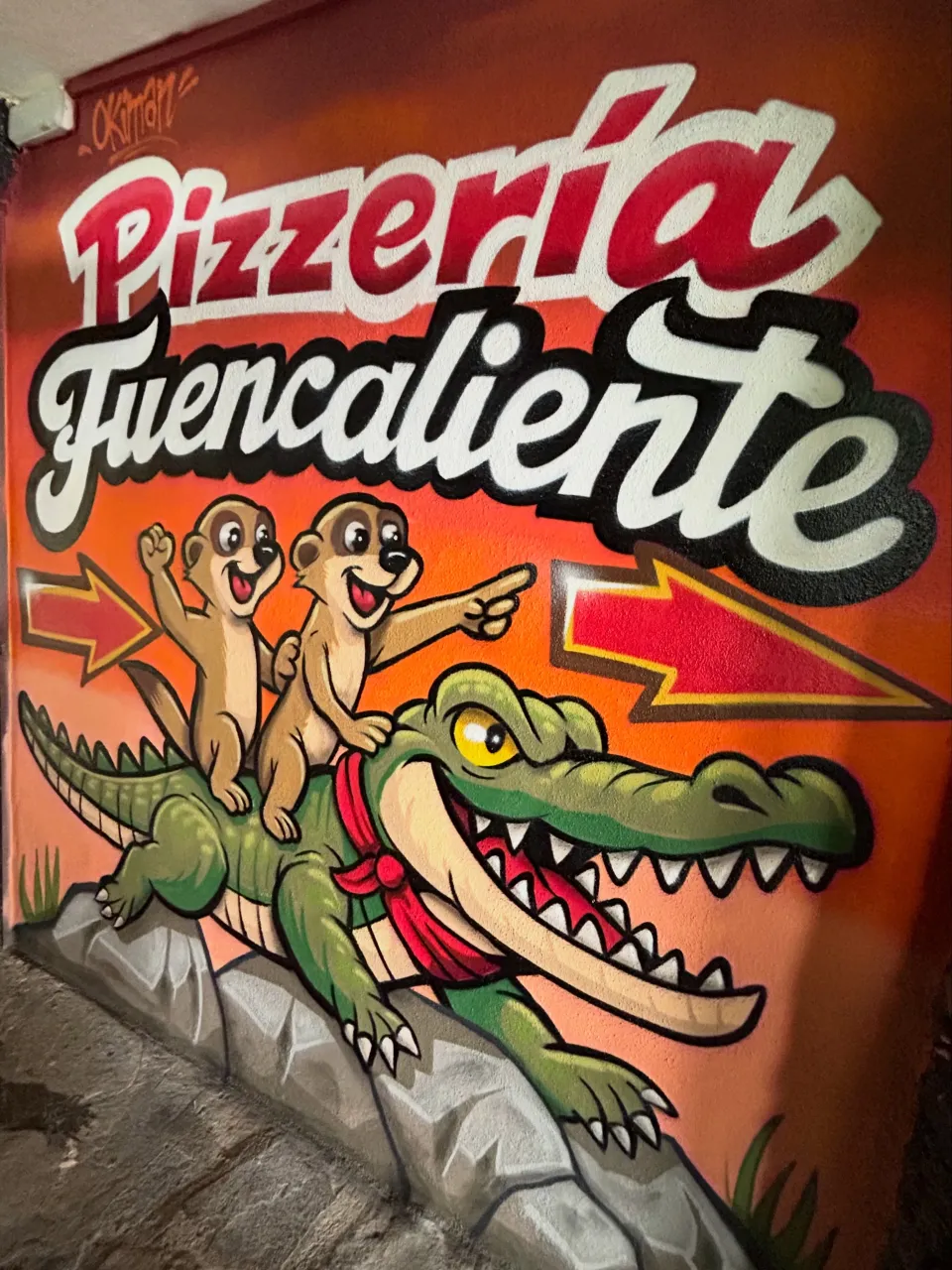 Mural de un caimán con dos suricatas a lomos y el rótulo Pizzería