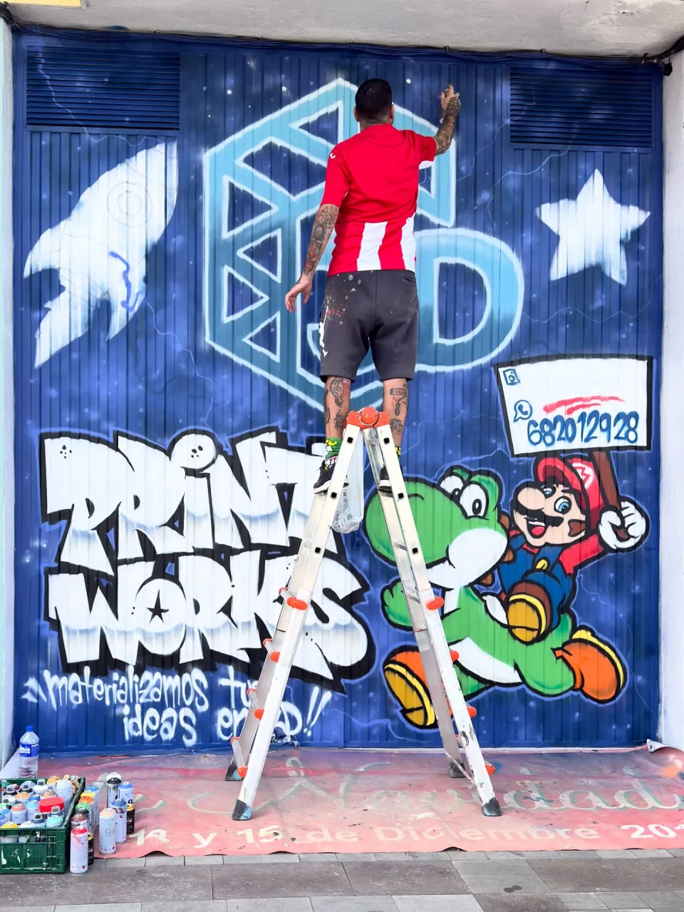 Okiman subido a una escalera pintando el logotipo 3D en el portón