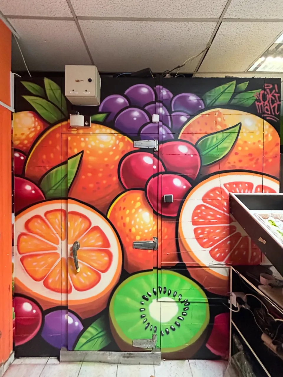 Puerta y pared de un local pintadas con naranjas, pomelos, uvas y kiwis