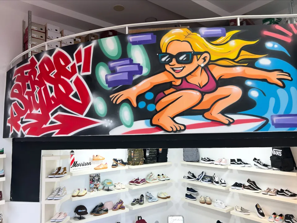 Mural de una surfista rubia sobre una ola, encima de los estantes de una tienda de zapatillas